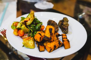 Beyaz yemek tabağında ızgara sebze ve biftek. Gurme sunumu, canlı ruh hali, yakın çekim, masa üstü görüntüsü, kapalı yemek ortamı, yemek dokusuna odaklanma, aşçılık ve sağlıklı konsept..