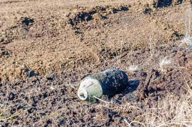 Bahar tarlası kazıları sırasında ıslak toprakta bulunan patlamamış eski bir bomba. Yakın çekim, yatay perspektif, yüksek gerilim havası, bozuk Peatland ortamında açık havada çekilmiş..