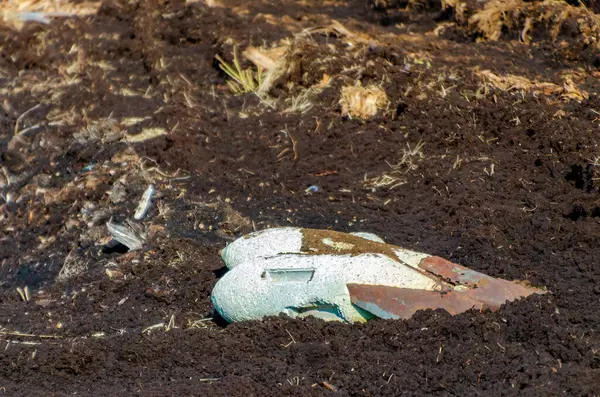 Paslı bomba mermileri soluk gökyüzünün altında unutulmuş savaş sonrası tarlasında sessizce yatıyor. Issız topraklarda terk edilmiş savaş kalıntılarının düşük açılı çekimi sessizlik ve ihtilaf sonrası bozulmaya neden olur..
