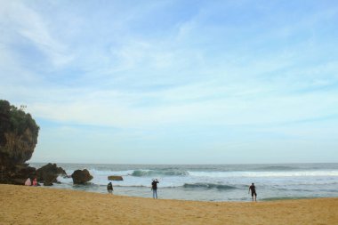 Gunungkidul, Yogyakarta, Endonezya - 14 Temmuz 2018 'den beri turistler, beyaz kum sahil şeridi boyunca uzanan kireçtaşı kayalıklardan Ngedan' ın doğal manzarasını karşılamaya hazırlanıyorlar..