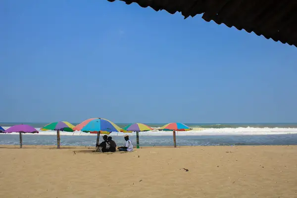 Yogyakarta, Endonezya - 10 Nisan 2021: Pok Tunggal 'ın beyaz kumlu kıyılarından renkli şemsiyelerin altına sığınan turistler var.