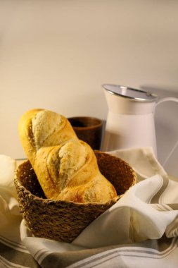 Hasır sepette ev yapımı taze ekmek. Arka planda süt için beyaz bir sürahi var. Havluda mis kokulu hamur işleri. Ekolojik kavram. Yandan görüntüle