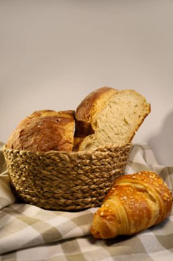 Hasır sepetteki ev yapımı taze ekmek, mis kokulu kruvasanın yanında. Havluda güzel kokulu pişirme. Ekolojik kavram. Yandan görüntüle