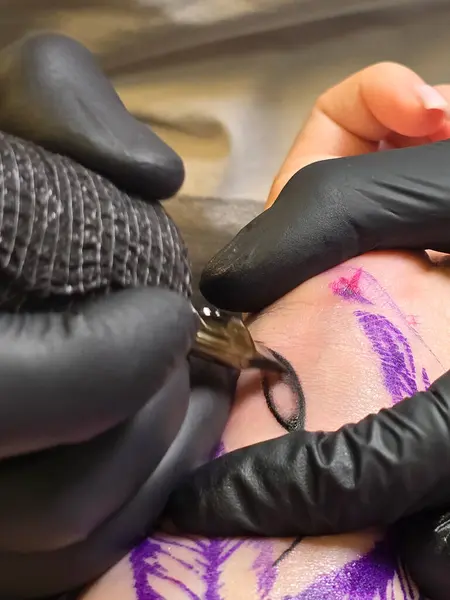 Eldivenli profesyonel yaratıcı dövme sanatçısı dövme salonunda genç bir kadına dövme yaptırıyor. Daktiloyla dövme yapma süreci.