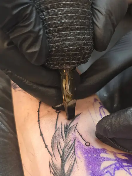 Eldivenli profesyonel yaratıcı dövme sanatçısı dövme salonunda genç bir kadına dövme yaptırıyor. Daktiloyla dövme yapma süreci.