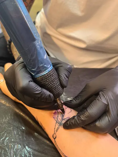 Eldivenli profesyonel yaratıcı dövme sanatçısı dövme salonunda genç bir kadına dövme yaptırıyor. Daktiloyla dövme yapma süreci.