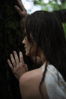 Genç bir kız bir nehrin kıyısındaki ağaç gövdesine tutunuyor.