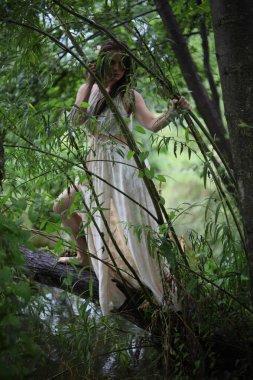 Nehir kıyısında, ağaçların yanında beyaz elbiseli genç kız.