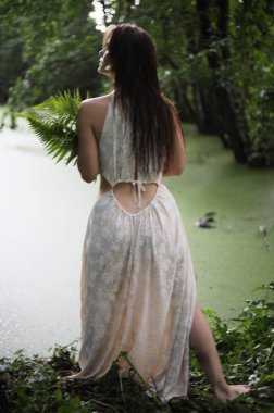 Nehir kıyısında elinde eğreltiotu olan beyaz elbiseli genç bir kız.