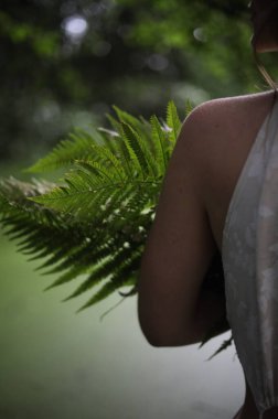 Nehir kıyısında elinde eğreltiotu olan beyaz elbiseli genç bir kız.