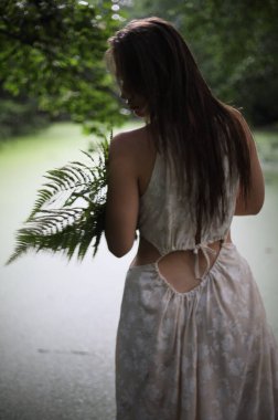 Nehir kıyısında elinde eğreltiotu olan beyaz elbiseli genç bir kız.