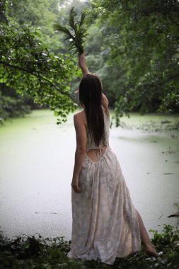 Nehir kıyısında elinde eğreltiotu olan beyaz elbiseli genç bir kız.