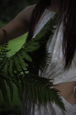 Nehir kıyısında elinde eğreltiotu olan beyaz elbiseli genç bir kız.