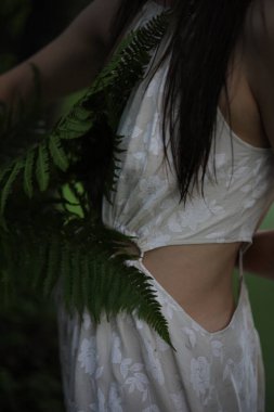 Nehir kıyısında elinde eğreltiotu olan beyaz elbiseli genç bir kız.