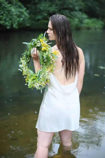 Beyaz elbiseli güzel bir genç kız, sarafan ve çiçek çelengi yazın nehirde ya da gölde