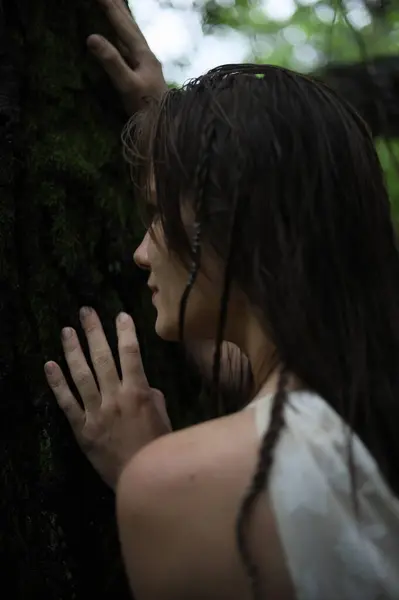 Genç bir kız bir nehrin kıyısındaki ağaç gövdesine tutunuyor.