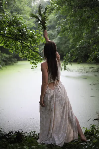 Nehir kıyısında elinde eğreltiotu olan beyaz elbiseli genç bir kız.