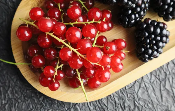 Siyah arka planda tahta bir tabakta farklı meyveler.