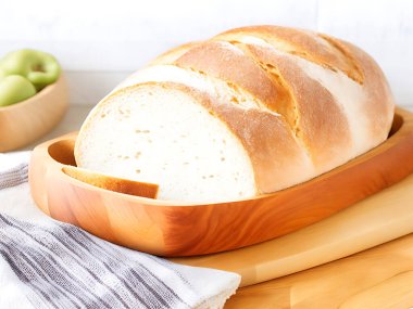 Arka planda ekmek sepeti olan bir somun ekmek kesim tahtasının üzerinde. 