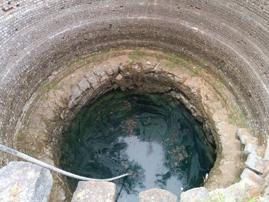 Eş merkezli halkaları olan antik taş kuyusu, inen basamaklar ve dipte enkaz dolu karanlık su..