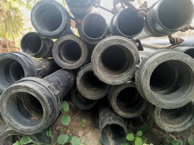 Arka planda kabataslak desen ve yeşillik olan siyah plastik boruların yakın çekimi.