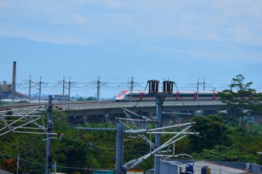 Endonezya 'nın yüksek hızlı treni Whoosh, endüstriyel ve dağ manzarası boyunca yükseltilmiş bir pistte modern demiryolu altyapısını sergiliyor..