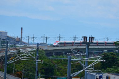 Endonezya 'nın yüksek hızlı treni Whoosh, endüstriyel ve dağ manzarası boyunca yükseltilmiş bir pistte modern demiryolu altyapısını sergiliyor..
