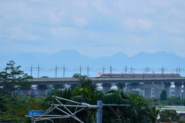 Endonezya 'nın yüksek hızlı treni Whoosh, endüstriyel ve dağ manzarası boyunca yükseltilmiş bir pistte modern demiryolu altyapısını sergiliyor..