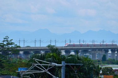 Endonezya 'nın yüksek hızlı treni Whoosh, endüstriyel ve dağ manzarası boyunca yükseltilmiş bir pistte modern demiryolu altyapısını sergiliyor..