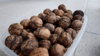 Döşeme yüzeyindeki cevizlerle dolu plastik konteynır. Fındıkla dolu plastik bir kabın yakın çekim görüntüsü, fayanslı bir yüzeye yerleştirilmiş.. 