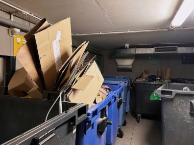Konut atık imha odasındaki aşırı geri dönüşüm ve çöp bidonları. Mavi kutuya istiflenmiş karton kutular, biyolojik, plastik ve karışık atık için diğer atık konteynırlarıyla çevrili..