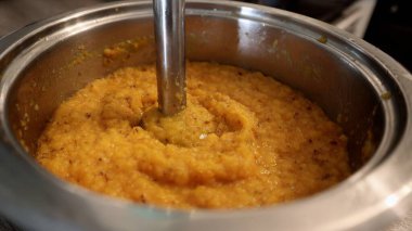 Yeni harmanlanmış portakallı mercimek çorbası veya sebze püresi ile dolu paslanmaz çelik bir tencerenin yakın görüntüsü. El blenderi karışıma batırılır ve pürüzsüz bir doku yaratır. Mutfak ortamında ev yapımı pişirme işlemi.