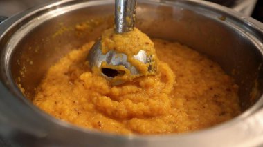 Taze pişirilmiş sebze püresi daldırma el blenderiyle karıştırılıyor. Kalın dokular ve canlı renkler sıcak bir ev yemeği atmosferini vurgular..