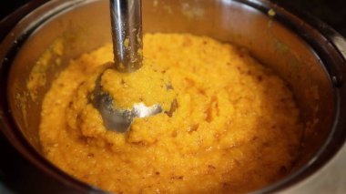 Kalın portakallı sebze püresi, el blenderi kullanılarak metal bir kaba karıştırılıyor. Sıcacık dokusu ve sıcacık rengi ev yapımı bir yemek olduğunu gösteriyor..