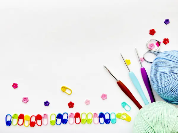 Beyaz arkaplanda iplik topları, örgü kancaları, makas ve dikiş izleri var.