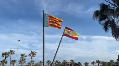 Bu görüntü İspanyol ve Valensiyalı bayrakların gururla dalgalandığını gösteriyor. Rüzgarda dalgalanan bayraklar denizin arka planına ve güzel gezinti güvertesine çarpıyor.