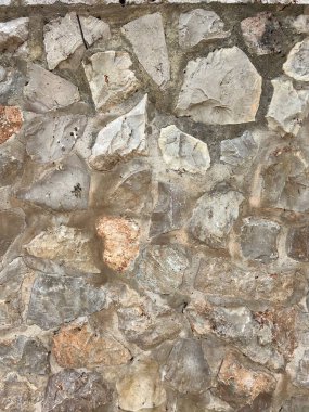 Bu resim, taştan bir duvar dokusunun yakın plan görüntüsünü sunuyor. Yüzeyde çeşitli şekillerde, boyutlarda ve toprak tonlarında yıpranmış taşlar sergileniyor, dayanıklı cazibe ve doğal çekicilik hissi somutlaştırılıyor.