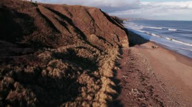İnsansız hava aracı kum tepeleri ve uçurumların üzerinden yükselerek Durham 'ın muhteşem sahil şeridini gözler önüne seriyor.