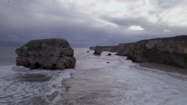 İHA yavaşça geri uçar ve Marsden Sahili 'ndeki kış fırtınası sırasında İngiliz kıyılarında yükselir.