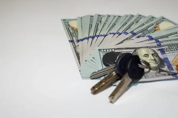 Bir dizi dairenin anahtarının yanına dizilmiş yüz dolarlık banknotlar servetin, mülkiyetin ve finansal yatırımın temalarını, yan görüşü vurguluyor