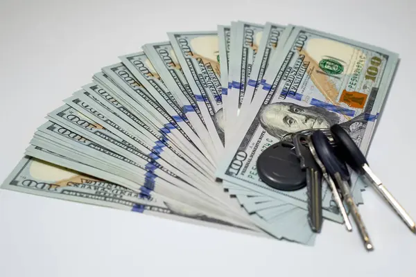 Bir dizi dairenin anahtarının yanına dizilmiş yüz dolarlık banknotların toplanması zenginlik, mülkiyet ve mali yatırım konularını vurguluyor.