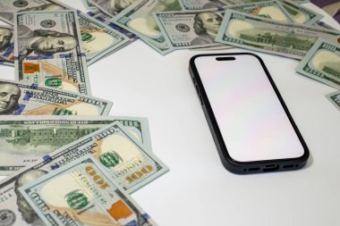 Yüksek değerli para birimi, zengin temalı bir düzende beyaz bir yüzey üzerinde akıllı bir telefonun etrafına yayılmış.