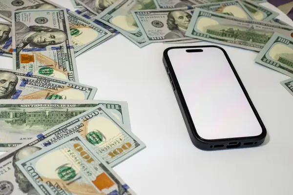 Yüksek değerli para birimi, zengin temalı bir düzende beyaz bir yüzey üzerinde akıllı bir telefonun etrafına yayılmış.