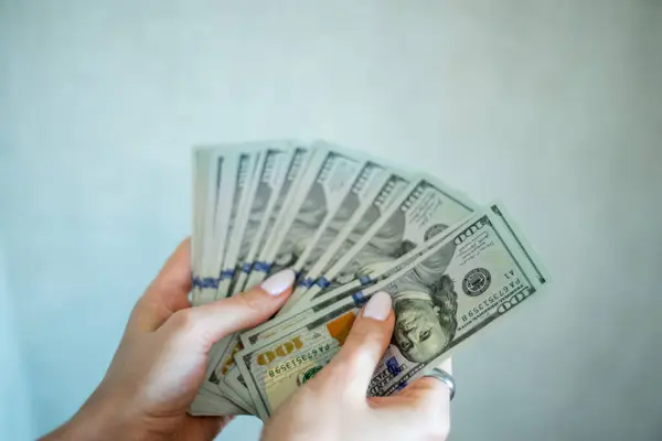 Eller birkaç yüz dolarlık banknotları tutar, zarif bir şekilde yayılır, kapalı bir alanda bir an için nakit taşıdığını gösterir. Finansal değişim ve zenginliğe odaklanmış durumda..