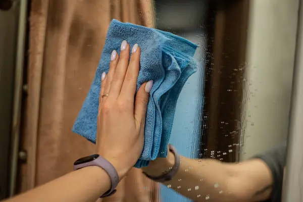 Bir kadının eli aynayı mikrofiber bezle siler, aynada yansıtır.