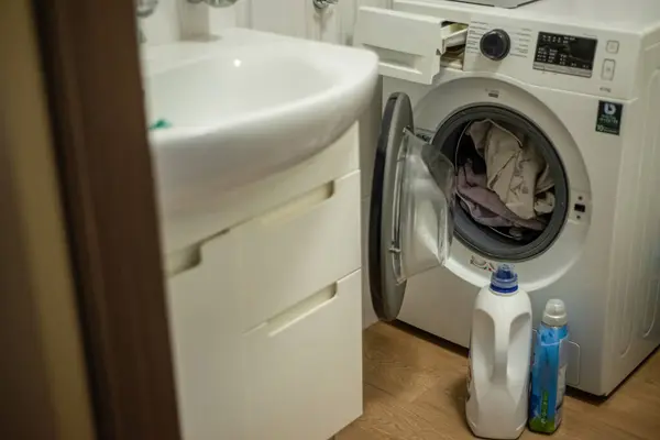 Çamaşır makinesi, çamaşır deterjanı ve temizlik malzemeleriyle dolu.