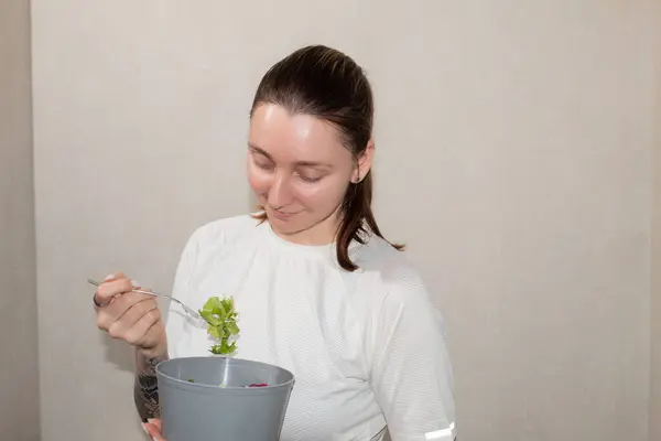 Genç kız mutfakta salata yiyor, sağlıklı besleniyor.