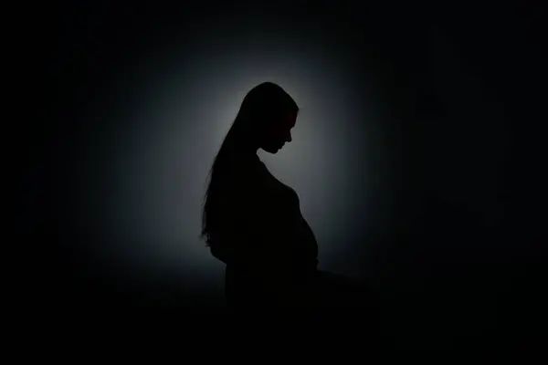 Beyaz arka planda hamile bir kızın koyu renk silüeti.