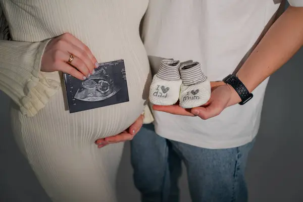 Genç bir aile, elinde ultrason ve ellerinde çocuk çorapları tutan bir çocuk bekliyor.