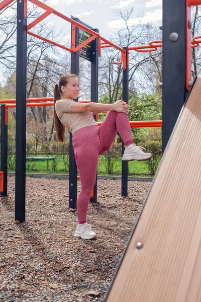 Genç bir kadın spor salonunda bacak ve kol hareketleri yapıyor, spor kıyafetler giyiyor, bahar havasında aktif ve sağlıklı kalıyor..